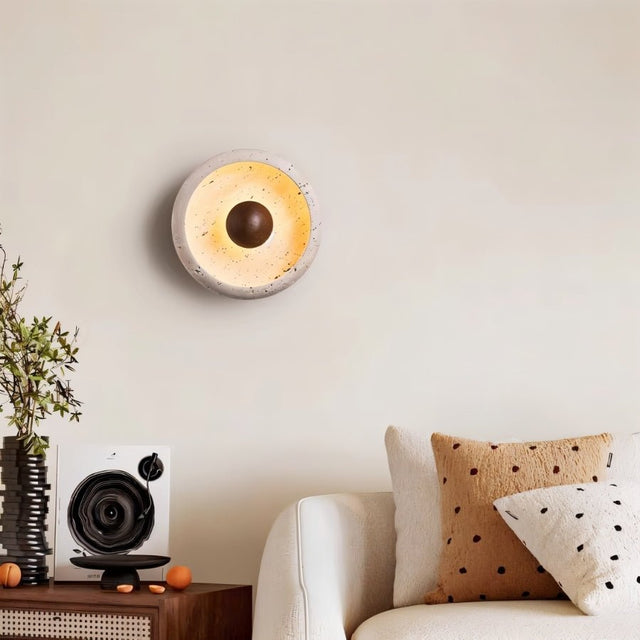 "A modern rustic wall lamp with a circular travertine frame and wooden centerpiece enhancing the decor of a contemporary living room."