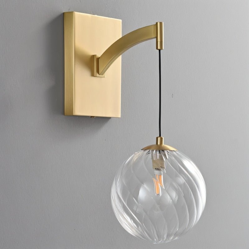 "A modern brass wall lamp featuring a rectangular backplate, a gently curved arm, and a spherical, clear glass shade with subtle ridges."