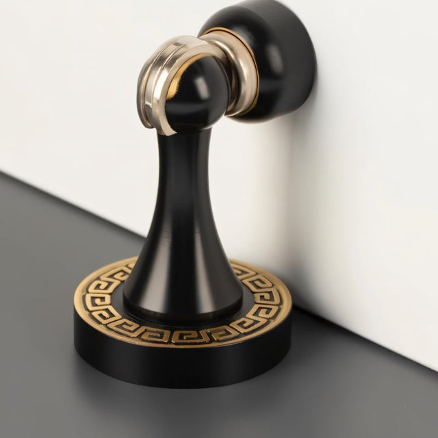 "Elegant, sculpted brass door stop with a black and gold finish, tapered design, and decorative base, installed on a wall to prevent door damage in modern and classic interiors."