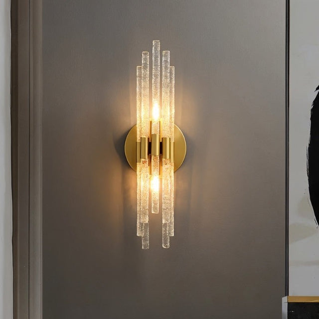 "A modern brass wall sconce with textured glass rods on a dark gray wall."