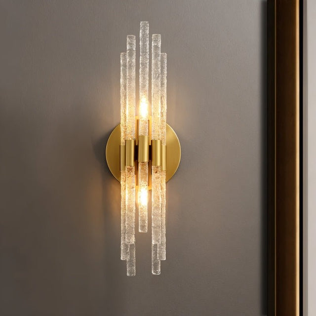 "A modern brass wall lamp with textured glass rods on a gray wall."