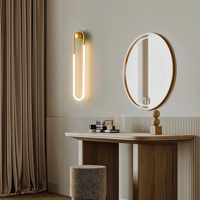"A modern, minimalist U-shaped wall lamp with a brass finish illuminating a bathroom vanity."