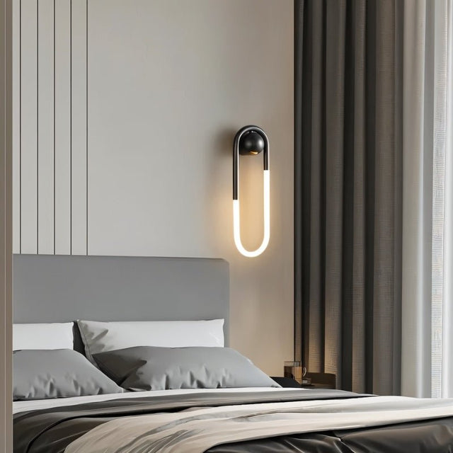 "A modern, minimalist U-shaped wall lamp with a black and brass finish illuminating a bedroom."
