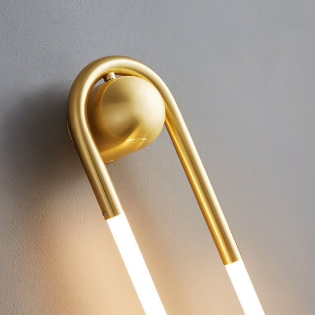 "Close-up detail of a modern, minimalist U-shaped wall lamp with a brass finish."