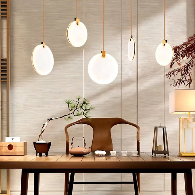 "Five alabaster pendant lights with brass accents hang at varying heights in a modern living room with a traditional Japanese-inspired table setting."