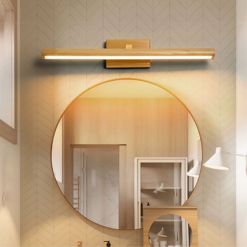 "A modern copper and natural wood wall lamp with a linear design, mounted above a round mirror in a contemporary bathroom with patterned wallpaper."