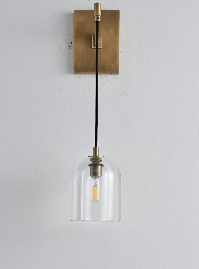 "A modern brass wall lamp with a bell-shaped clear glass shade, blending elegance and minimalist design with a curved arm and rectangular base."
