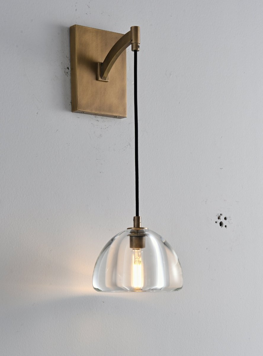 "A modern brass wall lamp with a curved arm and clear glass shade, blending elegance and minimalist design with a vintage touch."