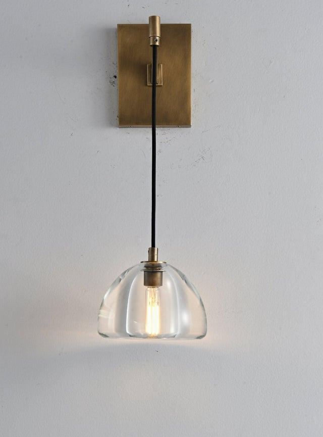 "A modern brass wall lamp with a dome-shaped clear glass shade, blending elegance and minimalist design with a curved arm and rectangular base."