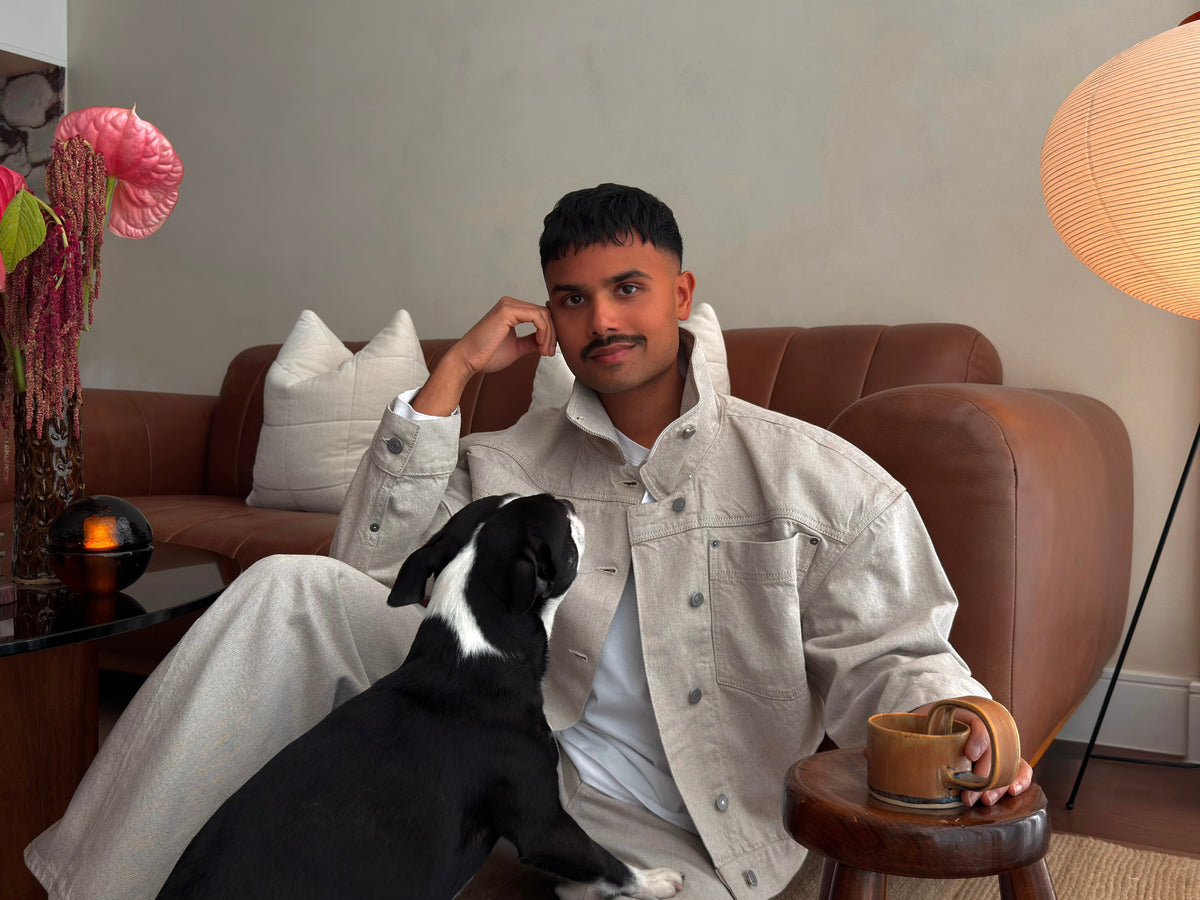 Home and hosting content creator Abhishek Dekate seated with his dog in his living room, surrounded by warm wood tones, sculptural lighting, and floral arrangements.