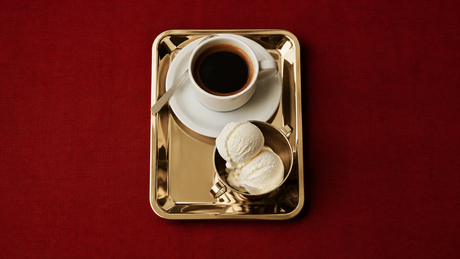 Affogato with vanilla ice cream and espresso served on a polished brass tray against a rich red background.