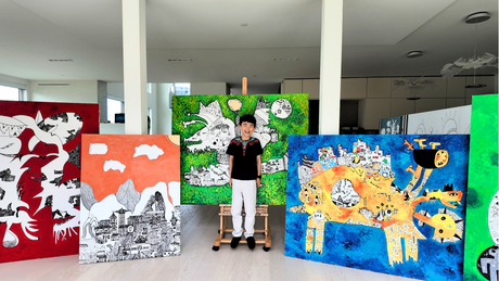 Young artist Jayden Ju stands smiling among several of his large-scale colorful paintings in a bright contemporary studio, showcasing his vibrant, imaginative artworks featuring abstract landscapes, fantastical creatures, and graphic illustrations.