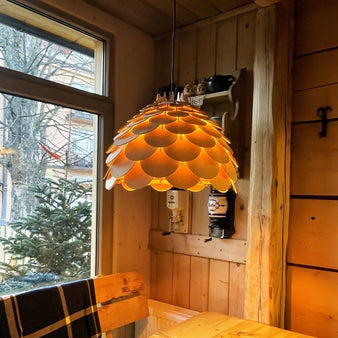 "The Atal wooden pendant lamp, glowing warmly, illuminates a rustic cabin interior with wood paneled walls and a window view of trees."