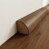 Curved wooden baseboard in rich brown finish, positioned against a light wall and floor.