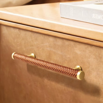 "Braided leather pull bar handle with a luxurious finish on a modern wooden drawer."