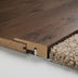 Close-up of a WPC flooring transition, featuring dark wood texture and a soft beige carpet edge with metal trim.