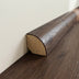Close-up of round wood trim molding with a dark wood finish and a lighter base against a beige wall.