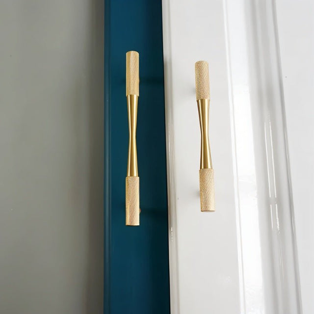"Two brass pull bar handles with knurled detailing on a white and blue paneled door, highlighting their cylindrical design."
