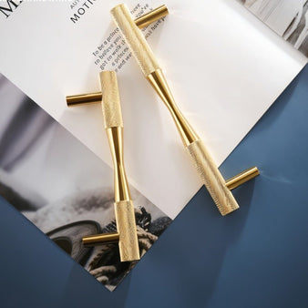 "Close-up of two brass pull bar handles with a cylindrical design and knurled detailing, placed on a magazine with text."