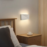"minimalist wall lamp in bedroom, white aluminum fixture, ambient lighting near wooden furniture, geometric design"