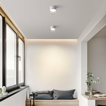 "A sleek, modern Hafra ceiling light installed in a living room with large windows, providing ambient lighting and enhancing the minimalist decor with its aluminum and glass materials."