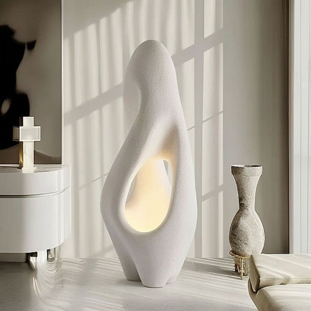 "Izbu Floor Lamp illuminated by natural sunlight, showcasing its sculptural design, smooth curves, hollow details, and polystyrene material in a modern setting."