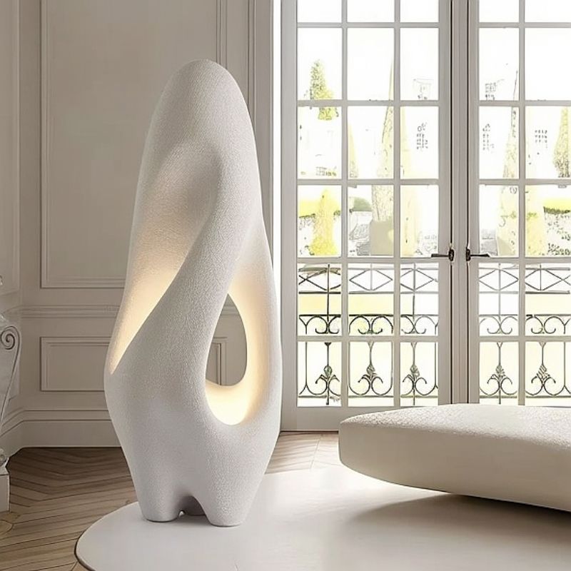 "Izbu Floor Lamp positioned by a window, highlighting its sculptural form, smooth curves, and hollow details with a soft ambient light, crafted from polystyrene."