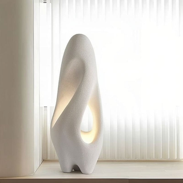 "Izbu Floor Lamp positioned near a window, highlighting its sculptural form, smooth curves, and hollow details, crafted from polystyrene material, providing ambient light."