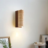 "Wall-mounted lamp with a cylindrical travertine shade and wood base, emitting a soft glow in a modern room."