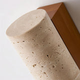 "Close-up detail of the textured travertine shade of a wall lamp, showing its natural variations and cylindrical shape."