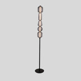 "The Lyris floor lamp with a black metal base and stacked translucent glass orbs emits a soft, ambient glow, making it a modern addition to any space. Constructed from metal, glass, and acrylic materials."