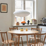 "Modern pendant light illuminating a cozy dining area with wooden chairs and table, minimalist decor by a window."