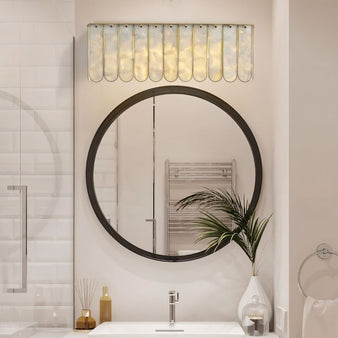 "Bathroom wall lamp with shell panels and metal frame, illuminating a round mirror and white vanity sink."