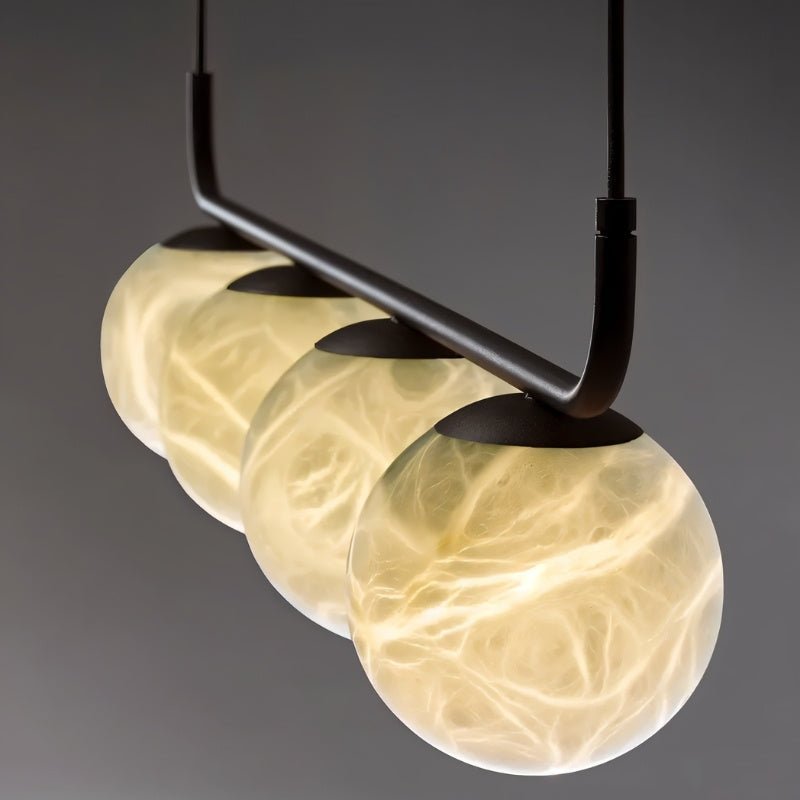 "Close-up view of the Ostra pendant lamp featuring three alabaster and aluminum spheres, showcasing a soft, diffused glow that enhances modern interiors with minimalist design."