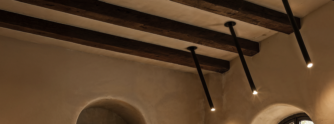 Ceiling with wooden beams and the Photine Ceiling Downlight in a room with a round window.