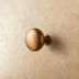 Round bronze cabinet knob mounted on a textured beige wall, showcasing a sleek and modern design.