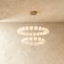 A modern chandelier with two tiers of white globes on gold hardware, hangs from a ceiling in a neutral-toned room.