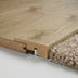Close-up of light wood flooring with a textured edge, resting next to plush beige carpet.