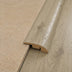 Image shows a close-up of a wood-look SPC flooring transition piece over a textured beige surface.