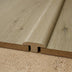 Close-up of a T-molding transition piece with a wood-like finish, fitting between two planks on a textured surface.