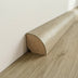 Rounded wooden baseboard in a light oak finish against a white wall and laminate floor.