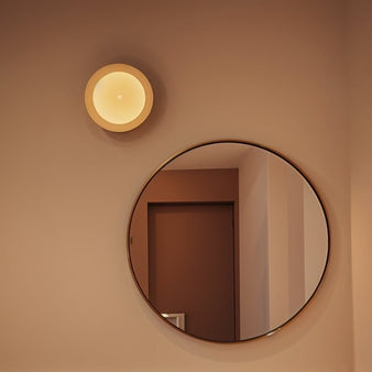 "Wall lamp with soft diffused light, wood frame, frosted glass, installed above a circular mirror in a modern room"