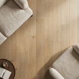Light oak wood-look plank flooring in a bright room with cream upholstered furniture and natural sunlight.