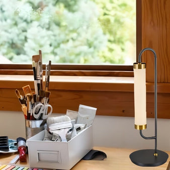 "Modern table lamp with a sleek glass cylindrical body and gold-tone metal accents on a desk setup"