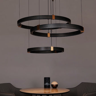 "Modern chandelier with three concentric aluminum rings, perforated surfaces, and acrylic diffusers, hanging above a table and chairs."