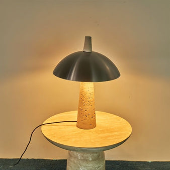 "Usra table lamp featuring an elegant dome-shaped aluminum shade and a travertine base, emitting soft, ambient lighting."