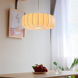 "Elegant pendant light with a pleated iron and silk design, softly illuminating a dining table with a warm, inviting glow."