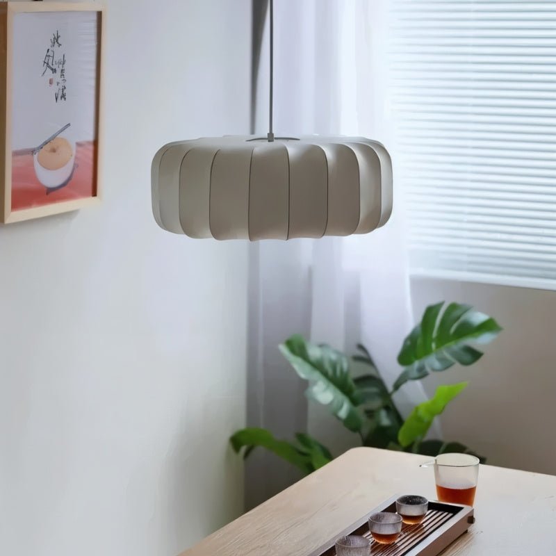 "Modern pendant light with a pleated design made from iron and silk, softly glowing and creating a cozy atmosphere in a contemporary setting."