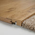 Close-up of wooden flooring with a textured beige carpet edge and metal transition strip. Natural finish, smooth surface.