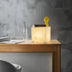 Square alabaster table lamp with a warm glow, books, and a yellow decorative figure on a wooden desk.